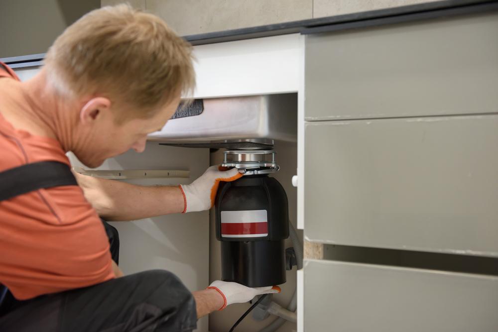 Technician installing a garbage disposal under a kitchen sink