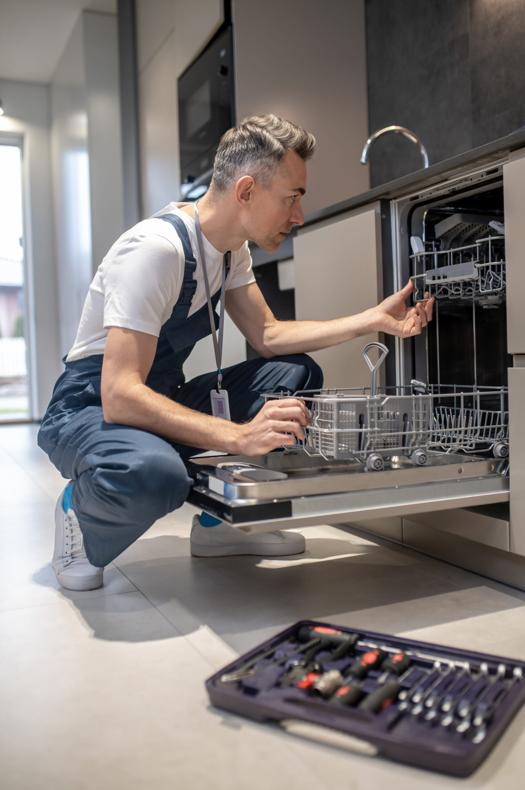Appliance repair technician inspecting and repairing a built-in dishwasher